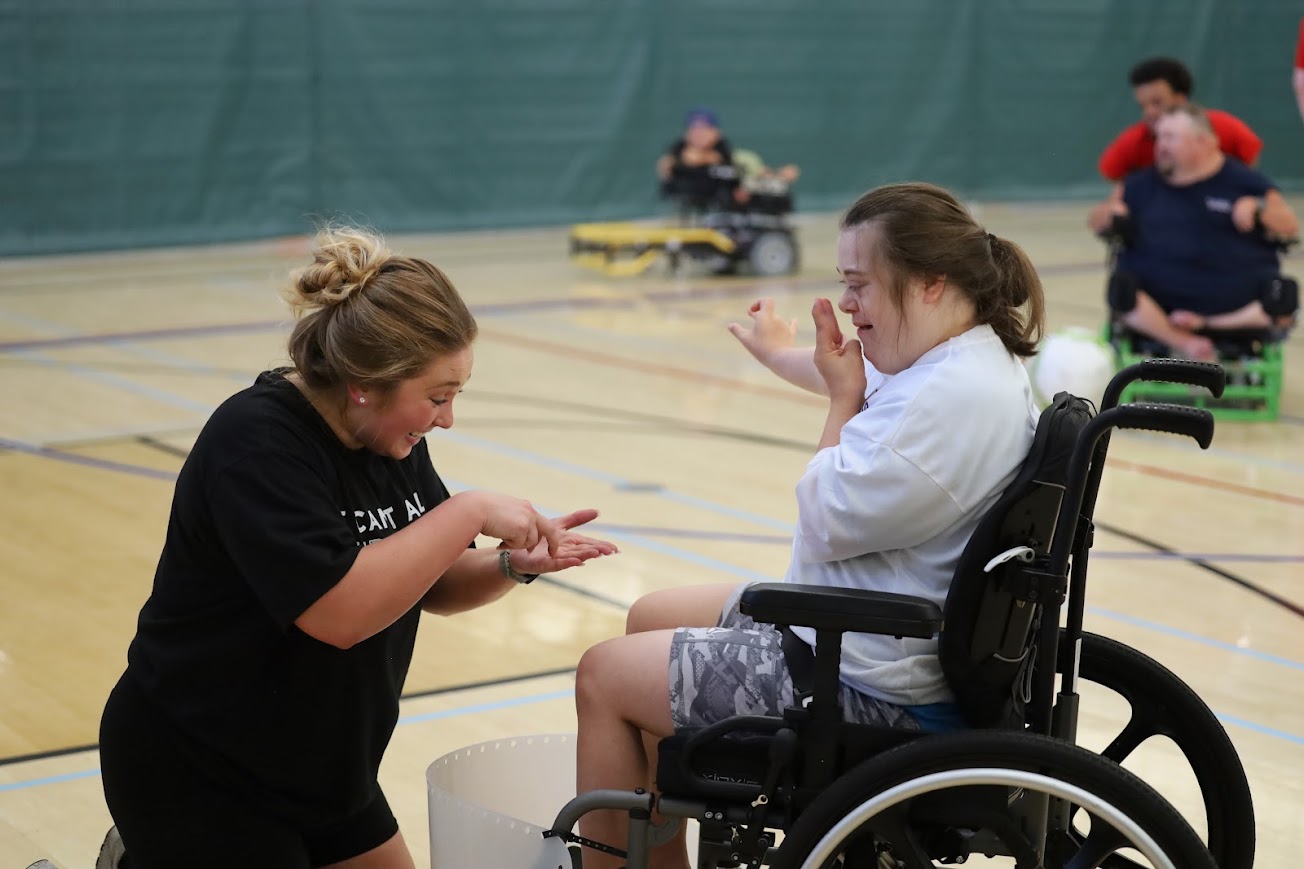 UASA President Joslynn Bigelow makes a powerchair participant laugh while gesturing with her hands
