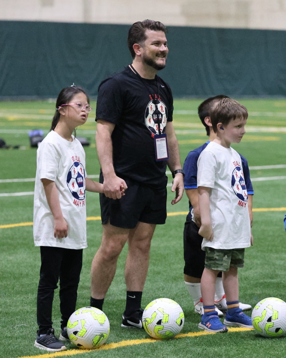 AYSO Coach Adam Webb, stands holding hands with two young TOPSoccer players, encouraging them as they ready themselves to begin a fun soccer drill