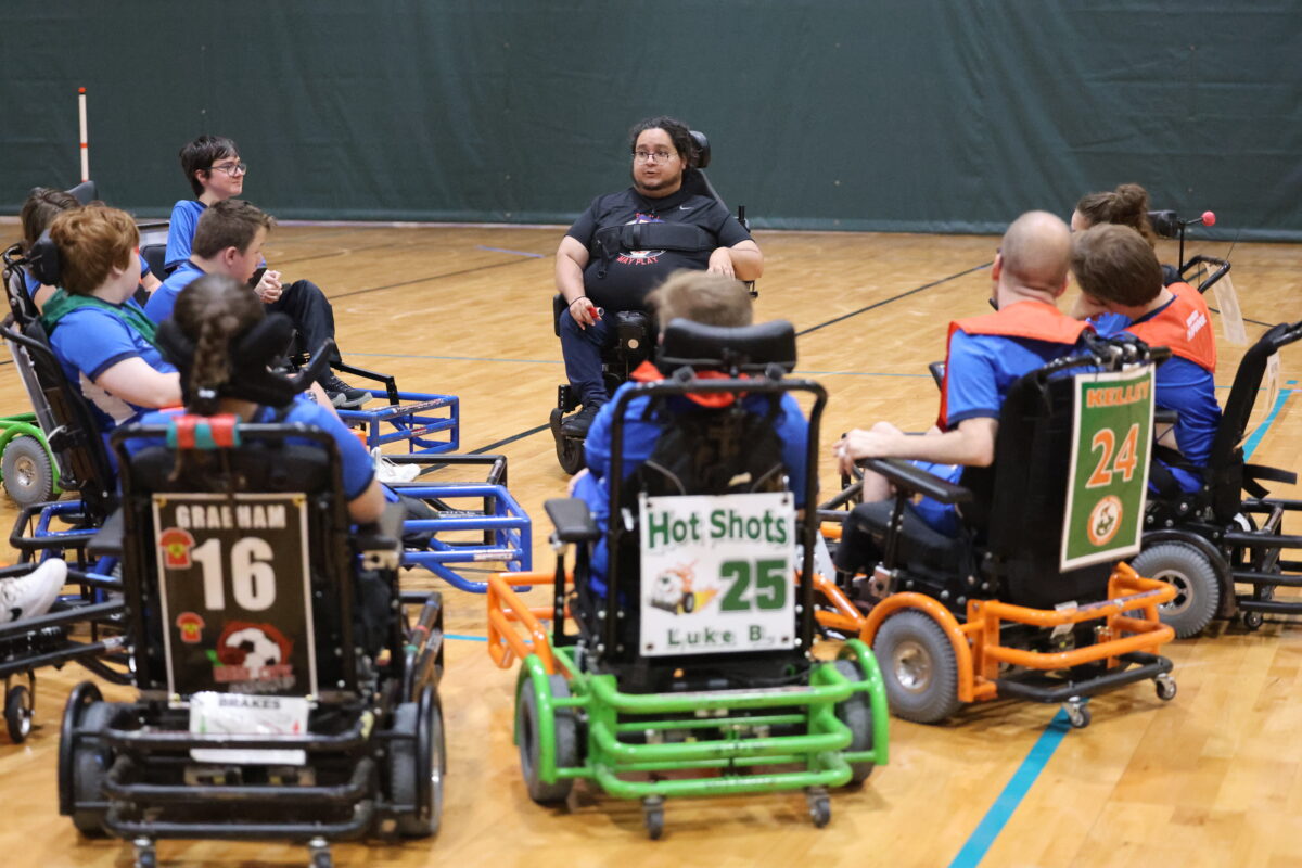 A group of power soccer players gather around to receive a team talk from their coach.