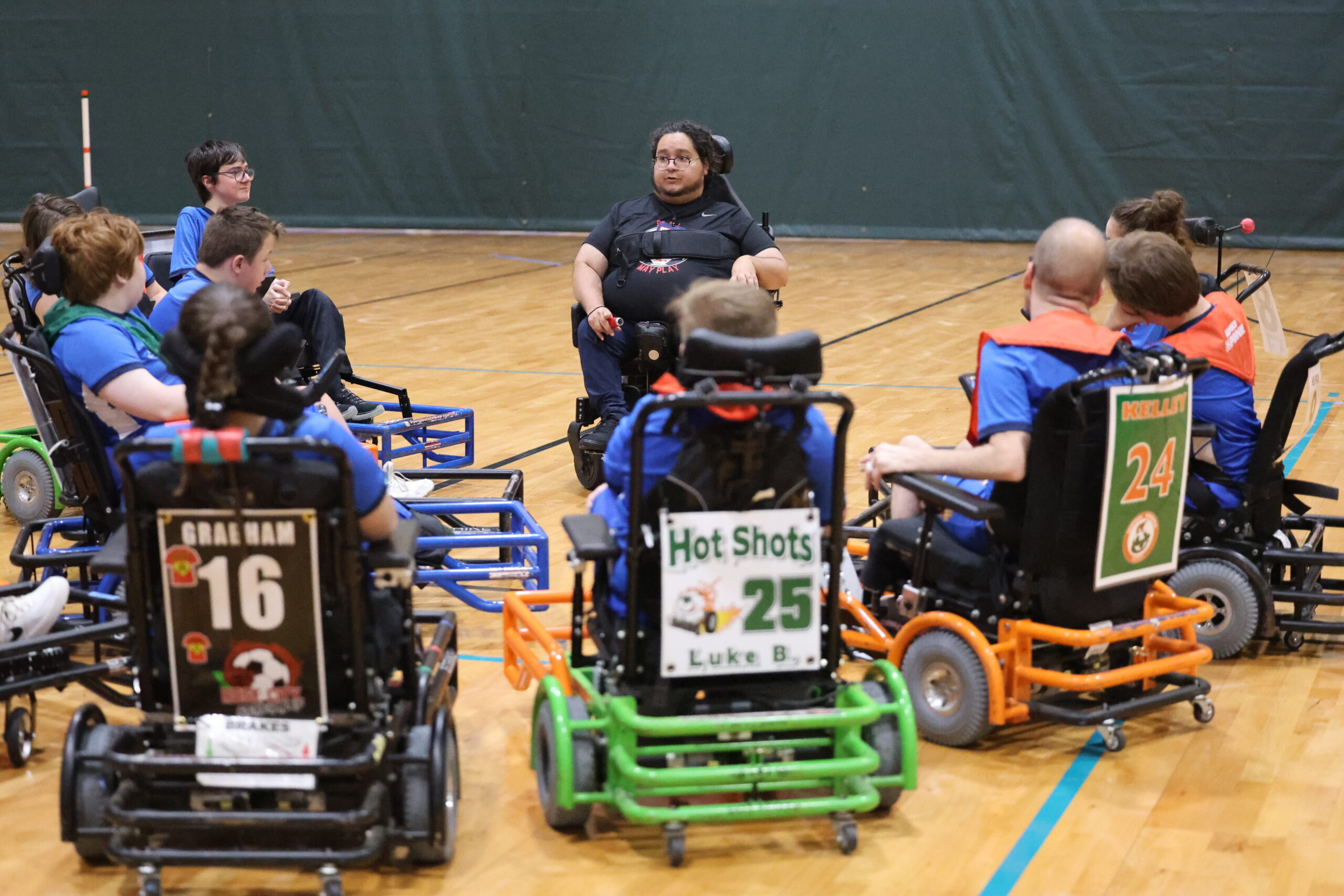 A group of power soccer players gather around to receive a team talk from their coach.